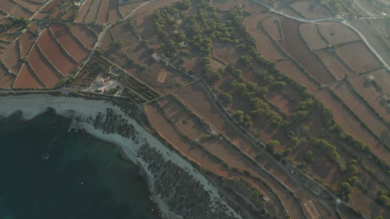 Rural Mediterranean Countryside fly over Brown dry Agriculture Fields revealing Factory by the Water on Malta Island, Sunset Aerial View