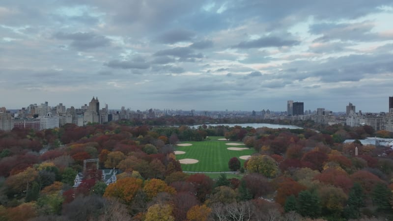 Forwards fly above Central park. The Great Lawn with baseball field and Jacqueline Kennedy Onassis Reservoir surrounded by autumn colour trees. Manhattan, New York City, USA