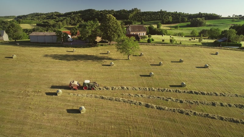 Aerial view of tractor harvesting straw bales in field.