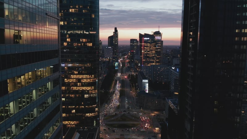 Narrow view between modern high rise downtown buildings on busy multilane road and large roundabout circuit. Twilight sky. Warsaw, Poland