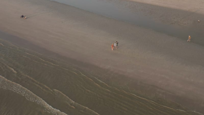 Aerial shot of friends walking along shoreline of beach in the Netherlands