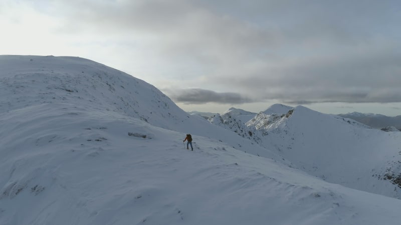 Mountain Climber Climbing Towards the Summit of a Snowy Mountain