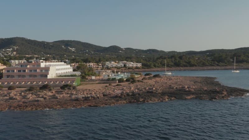 Aerial view of silent and calm ocean water flowing touching the shore with resorts and villas in a vacation home with yacht and boats parked in Ibiza in Spain