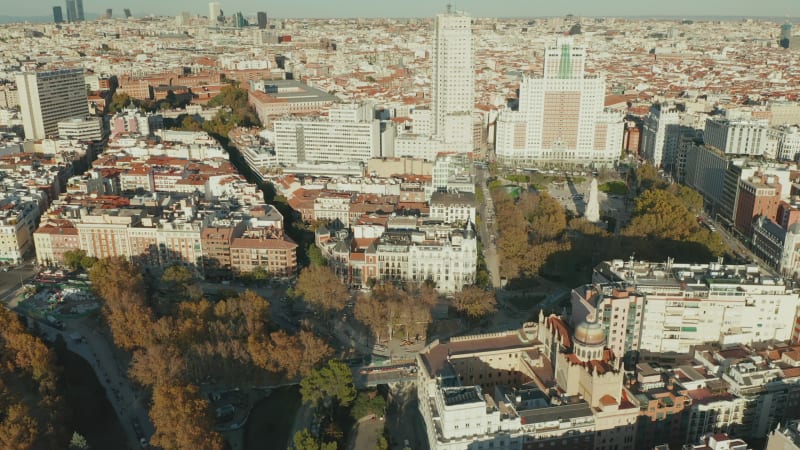 Aerial footage of town buildings in Plaza de Espana area lit by bright afternoon sun. Tilt up reveal cityscape.