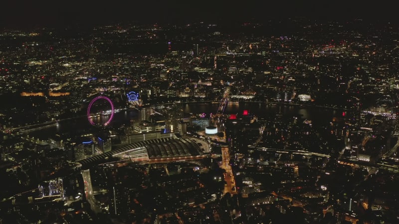 High angle view of Waterloo train station and London Eye at Thames river bank. Aerial panoramic shot of city at night. London, UK