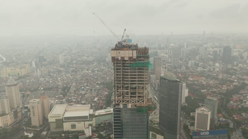 Aerial dolly shot tilting into overhead of tall skyscraper under construction in urban city center