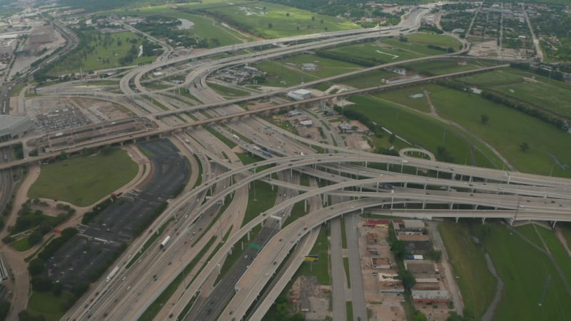 Aerial view of large and complex multi lane highway intersection. Cars smoothly driving in lanes through multilevel transport construction. Drone flying forwards and tilt down. Dallas, Texas, US
