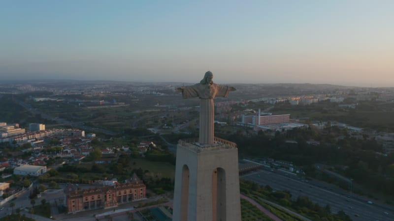 Aerial view of Christ the King Sanctuary in Almada in sunset time. Big Jesus sculpture standing on tall concrete pedestal. Lisbon, capital of Portugal.