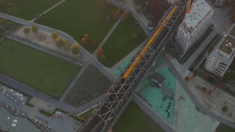 Iconic Typical Berlin Subway Train in yellow color passing a bridge through Public Park in Germany, Aerial Birds Eye Overhead Top Down View