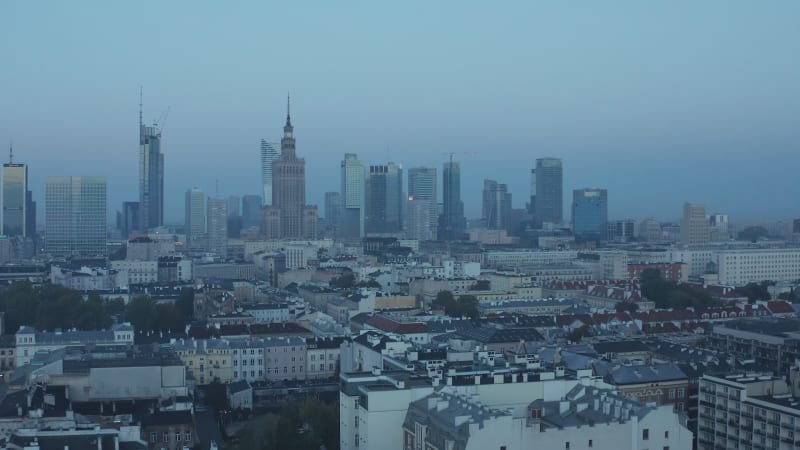 Backwards fly above urban neighbourhood. Skyline with skyscrapers in background. Aerial shot before sunrise. Warsaw, Poland