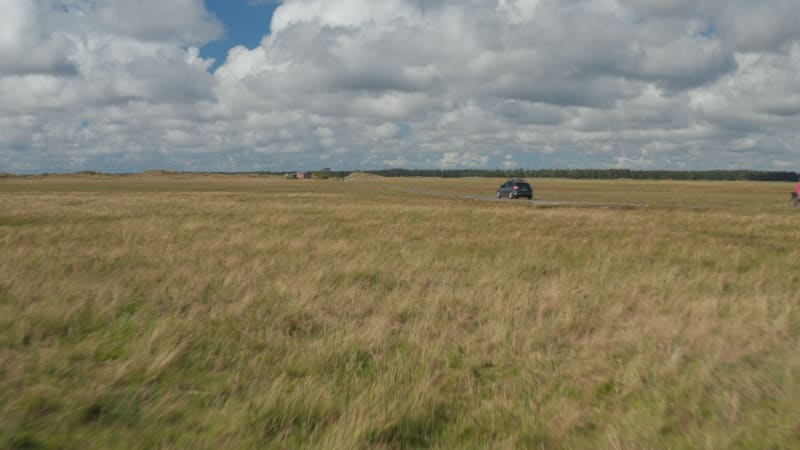 Drivers giving way to other cars and cyclists on narrow country road through vast flat grasslands. Denmark