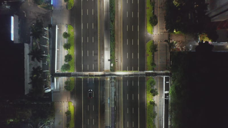 Birds eye overhead aerial view of lonely car driving down an empty highway during coronavirus lockdown in major city