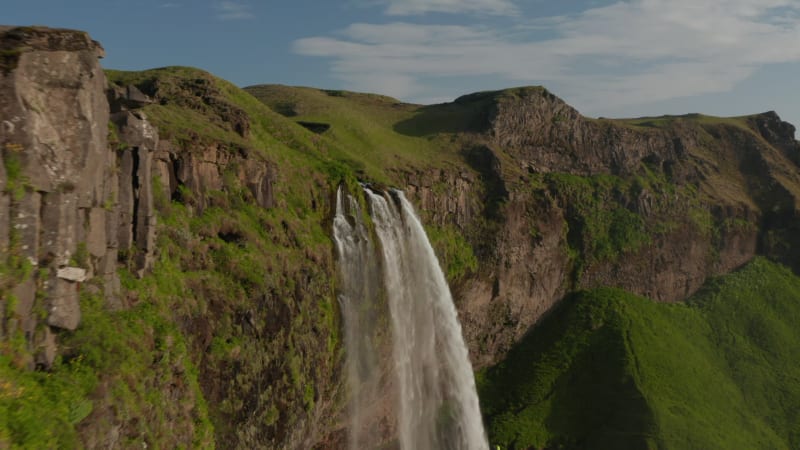 Birds eye flying over stunning Seljalandsfoss waterfall in Iceland south coast. Amazing drone view showing stone mossy cliff and water flowing cascade in highlands