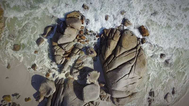 Aerial view of waves crashing on granite rocks on beach.