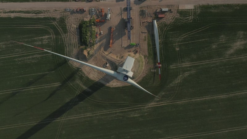 Close overhead drone view flight over Wind Turbine under construction being built on rich green agriculture field