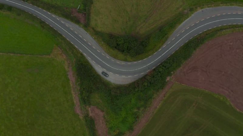 Aerial birds eye overhead top down ascending view of car standing aside road winding between fields and meadows in countryside. Ireland