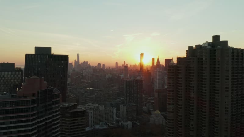 Forwards fly between high rise apartment buildings in city. View against colourful sunset. Revealing silhouettes of downtown skyscrapers in distance. Manhattan, New York City, USA