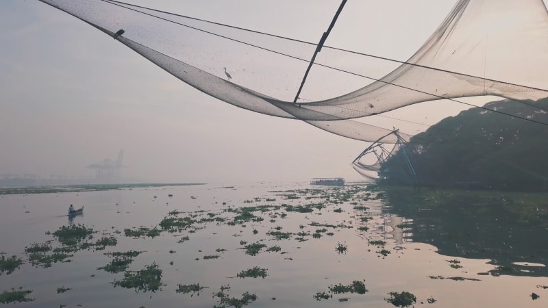 Flying under large fishing net with birds and people arriving on the boats