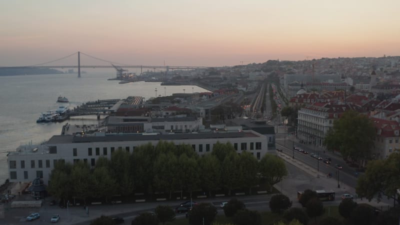 Aerial view of multi lane bus and car traffic in the evening on the coast of Lisbon, Portugal with Ponte 25 de Abril red bridge in the background