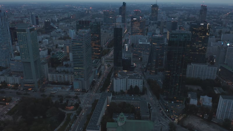 Descending shot of streets and high rise downtown buildings at dusk. Stream of cars driving on road. Warsaw, Poland