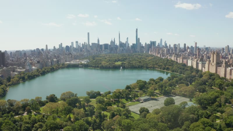 Central Park in Manhattan on a beautiful Summer Day with Blue Sky and Trees with Lake in Lush Green Forest and City Skyscrapers of New York City Skyline, Aerial Wide View