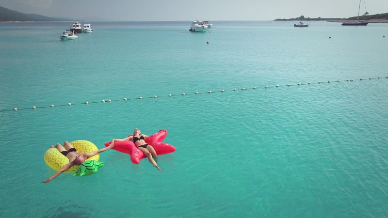 Aerial view of man and woman floating by string buoy on inflatable mattresses.