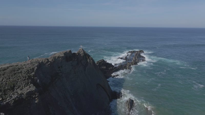 Aerial view of woman standing on cliff ledge over the ocean in