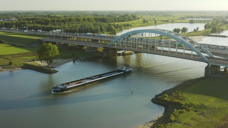 Transport ship sailing under a busy highway bridge