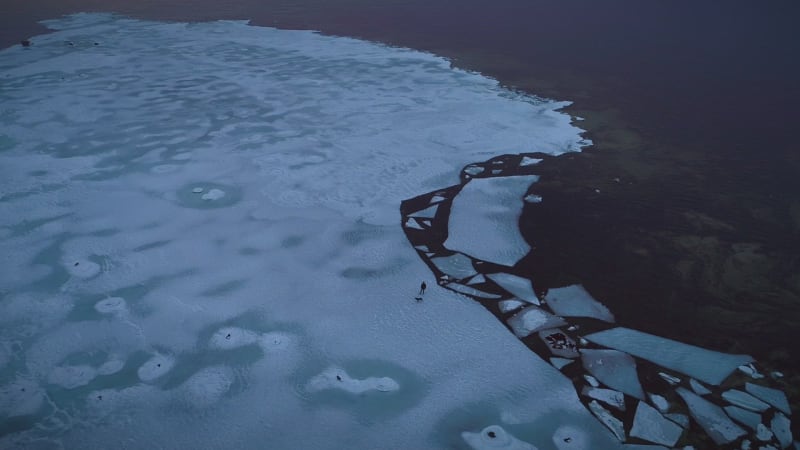 Aerial view of a man walking his dog on the frozen sea in Muraste.