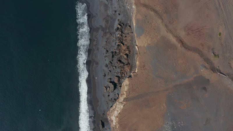 Top down flying towards amazing black beach in Iceland. Overhead birds eye of spectacular coastline with rocks and black volcanic sand