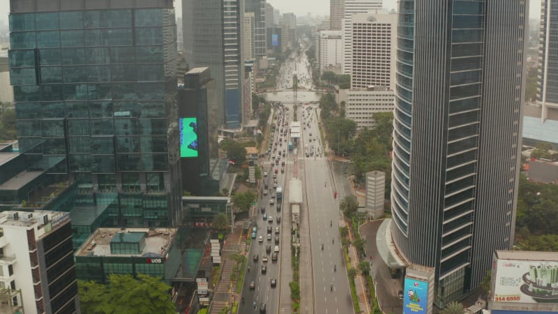 Aerial pedestal shot ascending between two skyscrapers of vehicles on a busy multi lane motorway in modern city center of Jakarta