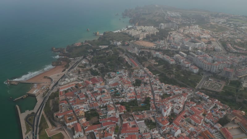 Astonishing aerial drone view of Lagos city landscape with paradisiac coastline in distance, Algarve, Portugal, tilt up, day