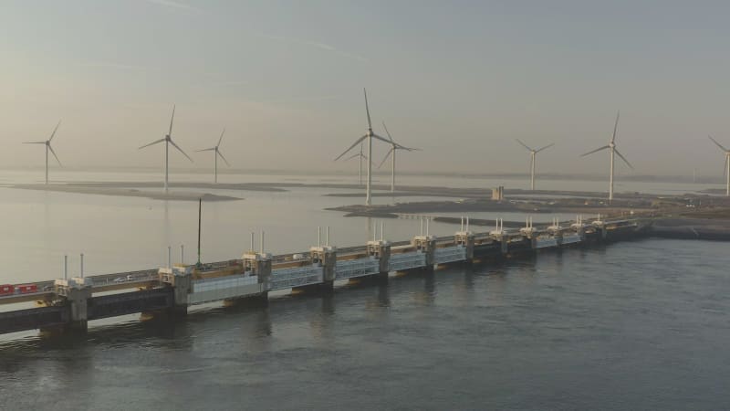 Cinematic aerial footage of a windmill in the sea with bridge in front