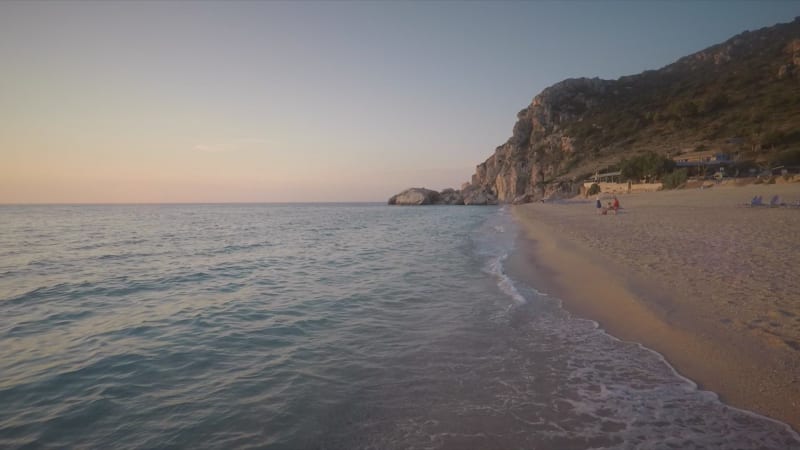 Aerial view of shore of the beach at sunset with few people.