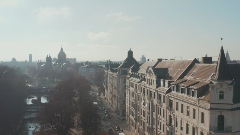 Beautiful residential street with old architecture apartment buildings by the Isa River in Munich, Germany on Sunny day, Aerial Scenic Slide left revealing City Skyline