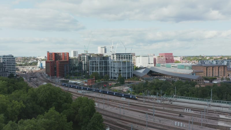 Aerial view of train unit leaving train station on multi track railway line. Modern apartment buildings around track. London, UK