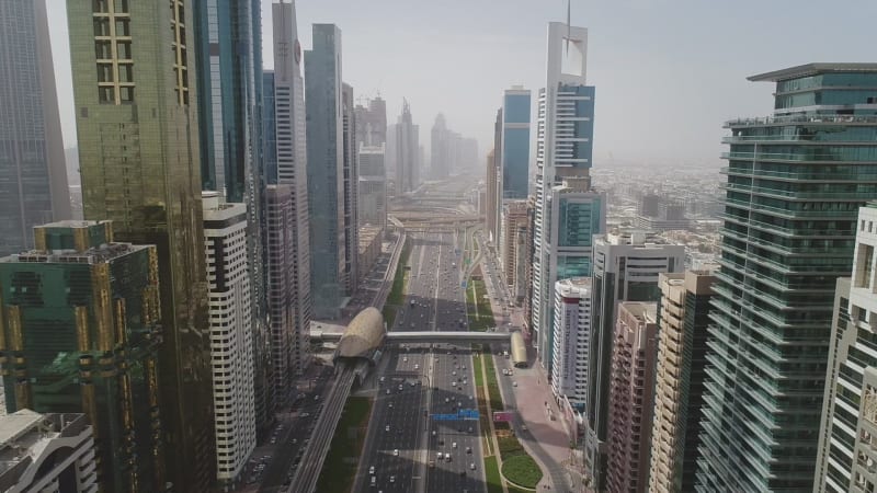 Aerial der farbenfrohen Wolkenkratzer Dubais und einer langen, stark befahrenen Straße.