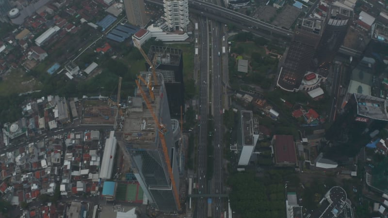 Aerial tilting dolly shot of tall skyscraper under construction revealing city skyline in the background