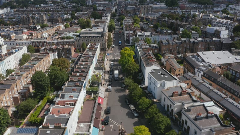 Forwards fly above long straight street. Townhouses along street in urban neighbourhood. Tilt up reveal skyline with skyscrapers. London, UK