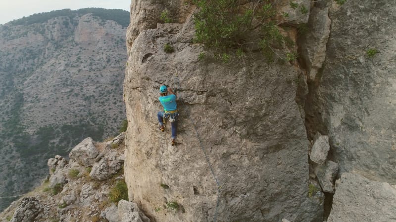 Aerial view of man climbing a stone mountain with safe equipment.