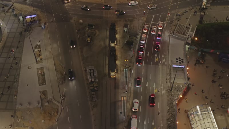 Descending and tilt up footage of vehicles driving through road intersection in evening rush hour. Warsaw, Poland