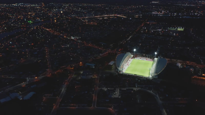 Amazing aerial shot of bright football arena contrasting with night city. Bright light shining on green football playfield. Limerick, Ireland