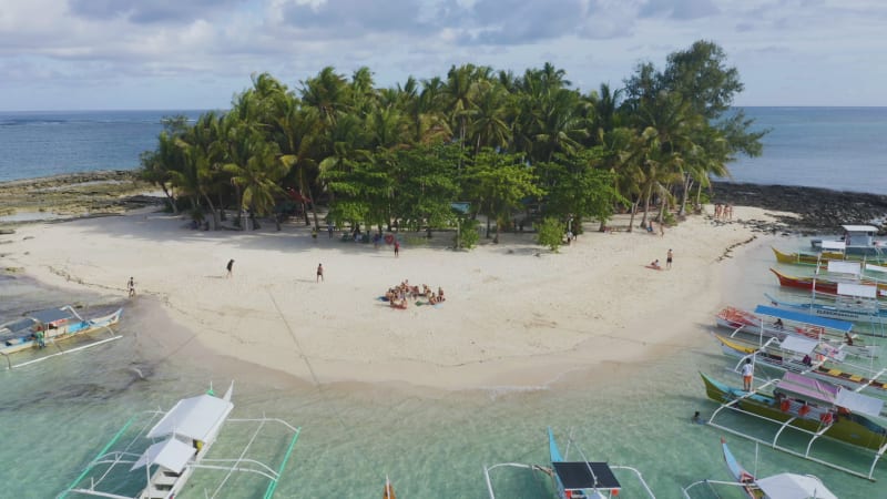 People on beach with boats lining tropical island in Philippines