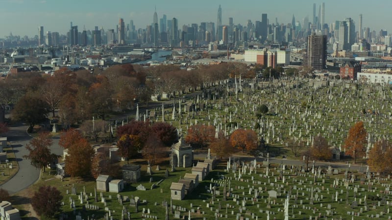 Aerial view of historic tombstones on Calvary Cemetery. Tilt up reveal of skyline with Manhattan skyscrapers. Queens, New York City, USA