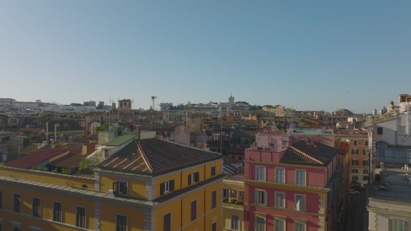 Low flight above old multistorey residential houses in urban borough. Colour facades lit by morning sun. Rome, Italy