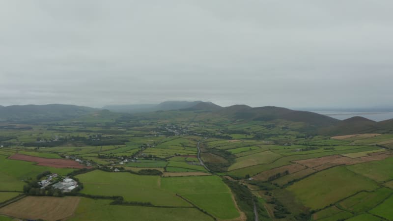 Aerial shot of green fields and meadows in countryside on cloudy day. Landscape panorama with hills in background. Ireland