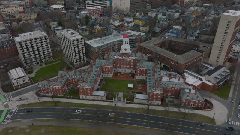 Aerial descending footage of Dunster House with grassy yard and red topped central tower. Revealing busy road on river bank. Boston, USA