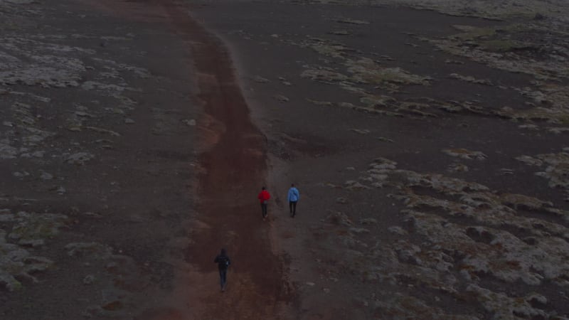 Aerial view three traveler adventurous hikers walking pathway in desert landscape in Iceland. Drone point of view of three explorer enjoying healthy lifestyle in isolated highlands