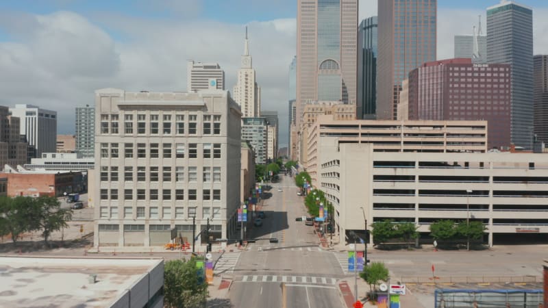 View from forwards flying drone above street downtown heading to group of skyscrapers. Elevated view low traffic on road. Dallas, Texas, US