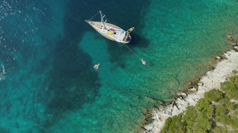 Aerial view of two women floating on inflatable next to sailing boat.